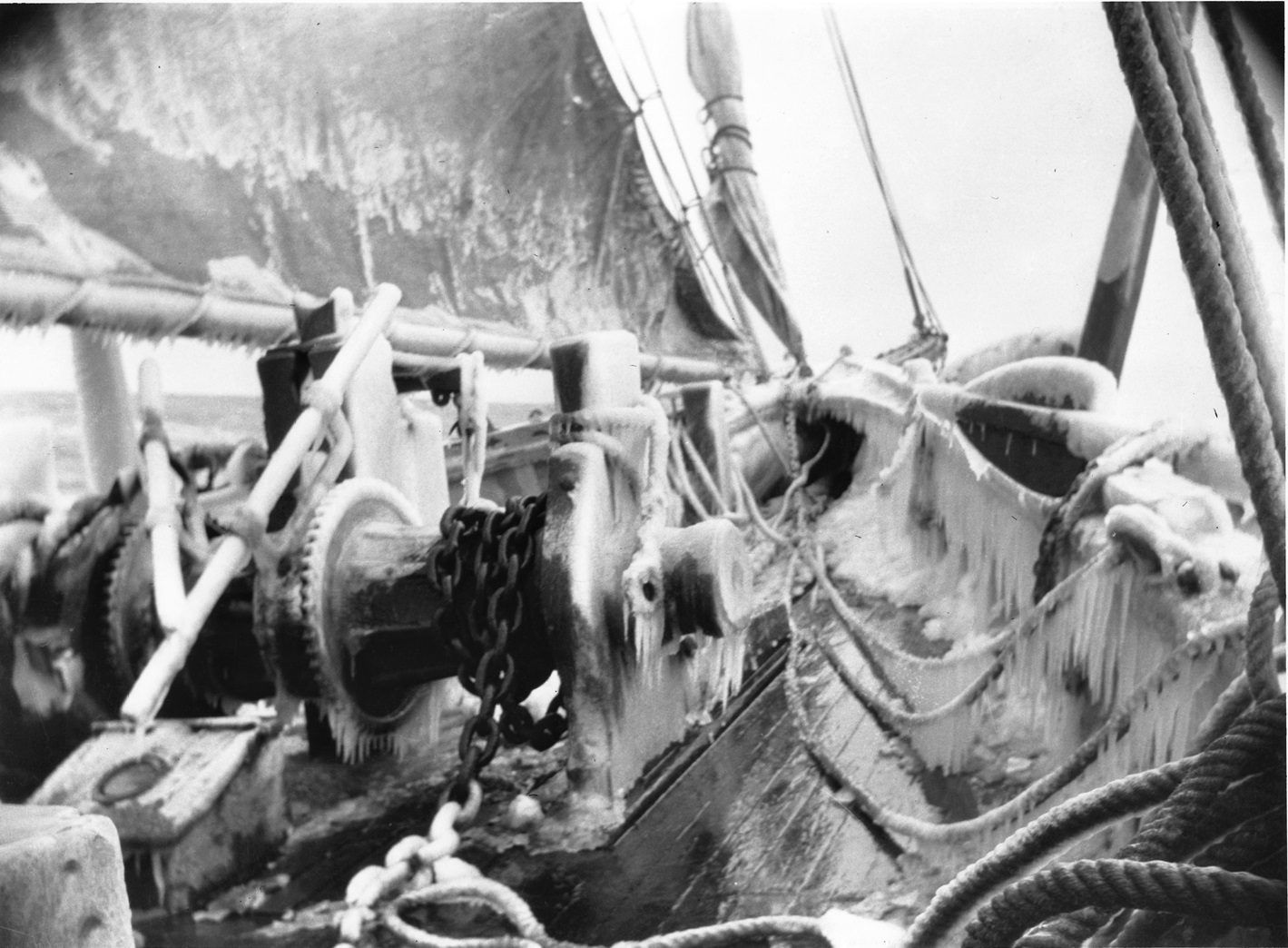 Iced Up Black-and-white photo of a schooner’s deck coated in thick ice. Icicles hang from the winch, anchor chain, railings and ropes, and the sail above is crusted with frost.