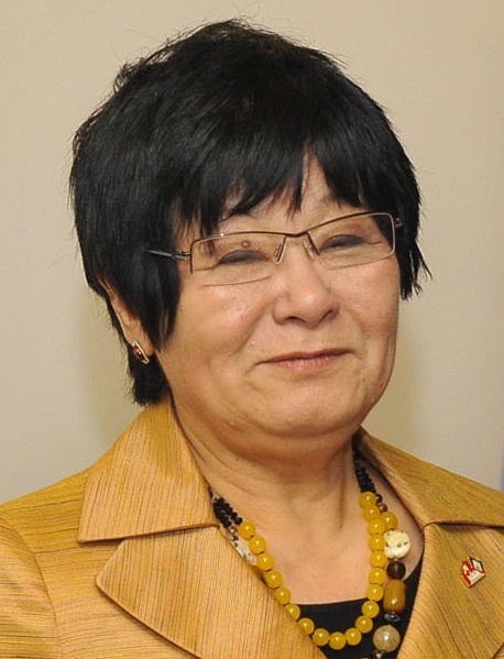 Une femme aux cheveux noirs, portant des lunettes et un costume jaune.