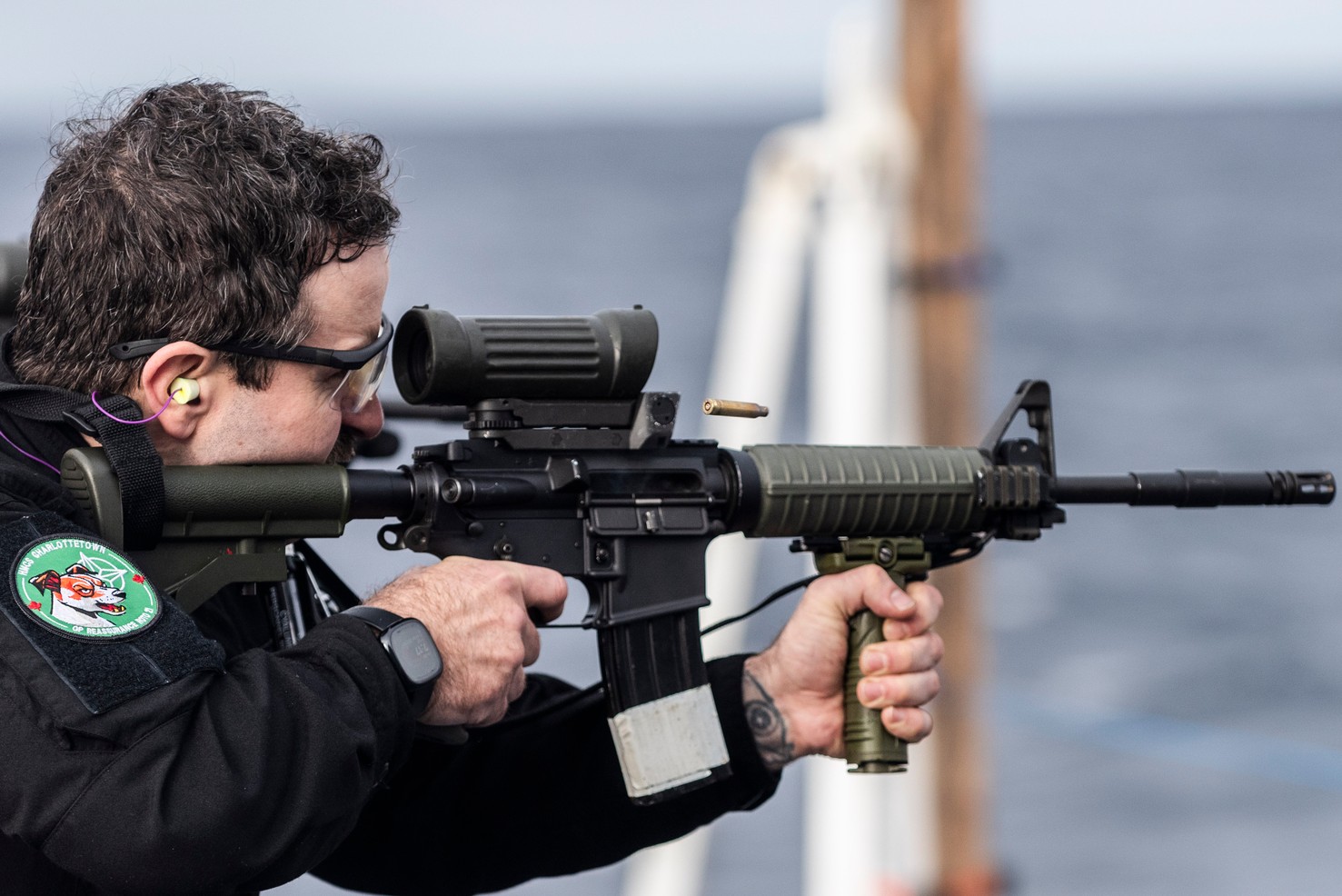Sailor firing a C8A3 carbine (2024) A sailor in a black uniform fires a C8A3 carbine with an optic and a vertical grip toward the sea.