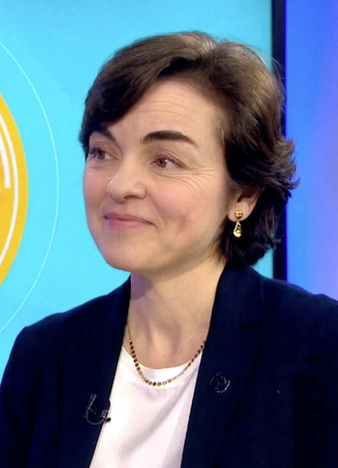 Christine Fréchette (2024) A white woman seen with a golden earing and necklace. She is wearing dark blue and white clothing.