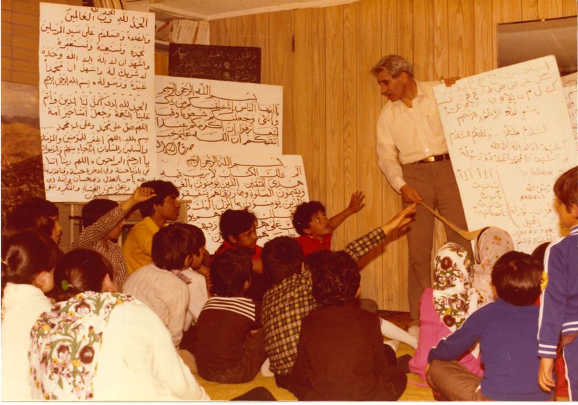 Fuad Sahin Teaching Children A man in a white shirt alongside some white signs with letters teaches a room full of children