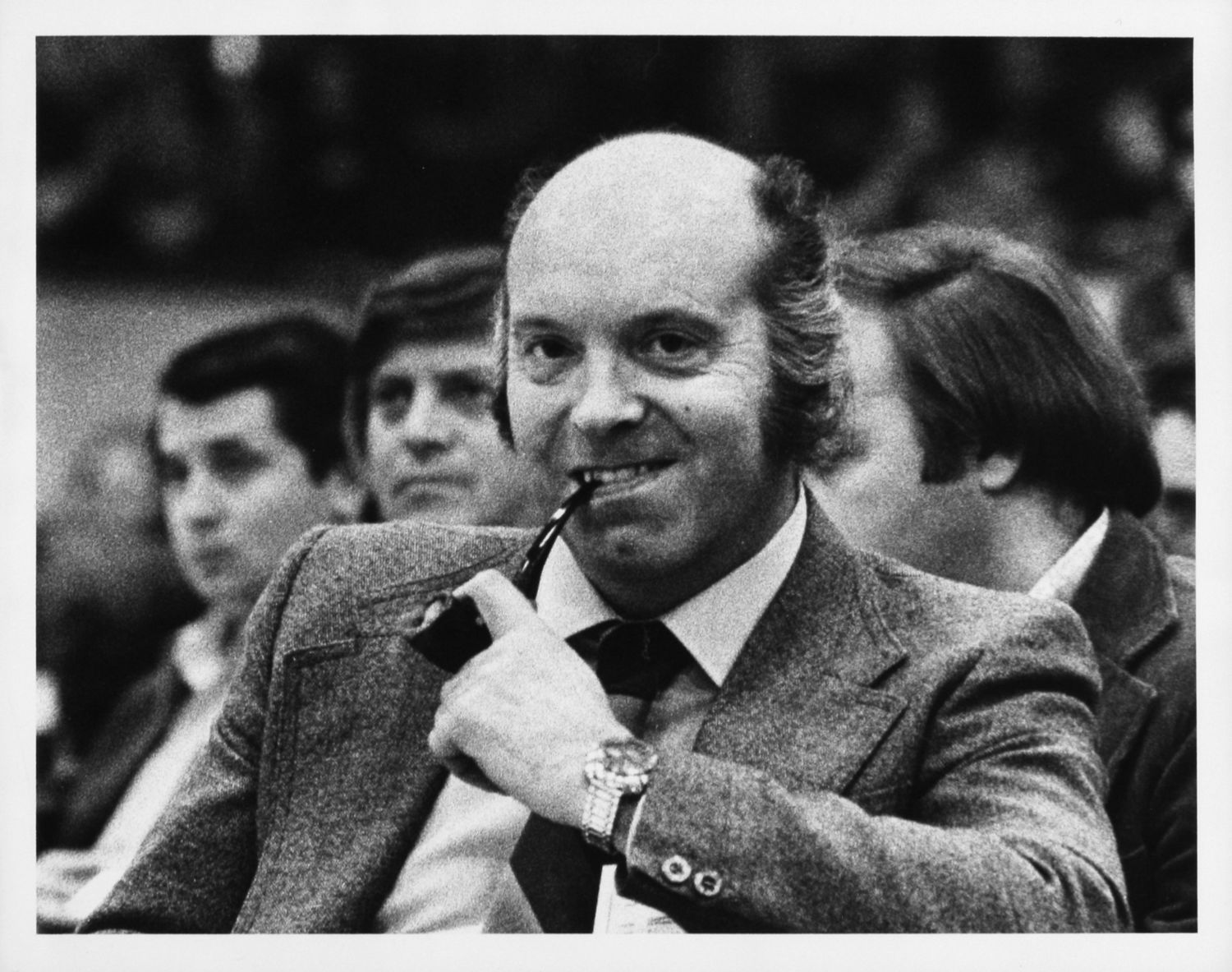 Photo en noir et blanc d'un homme souriant, une pipe à la bouche.