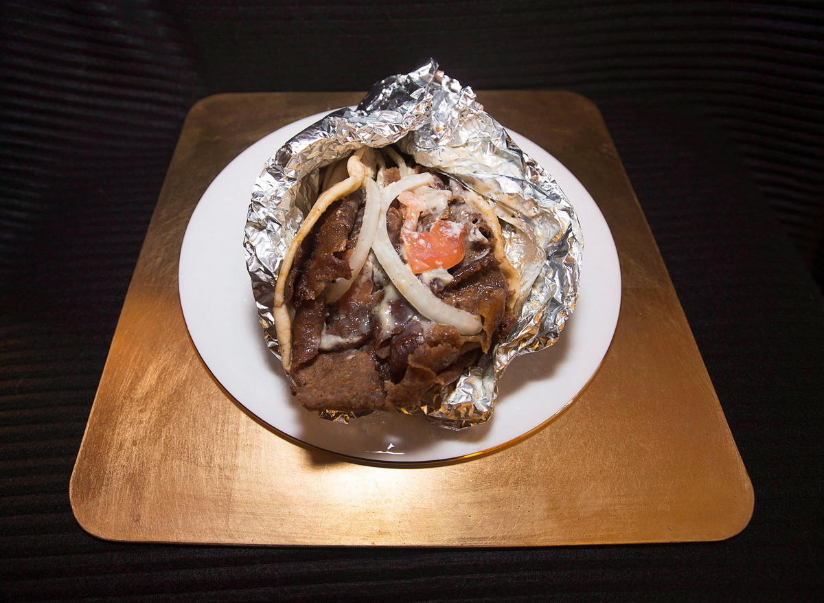 Halifax donair wrap wrapped in aluminium foil on a white plate on a brown table.
