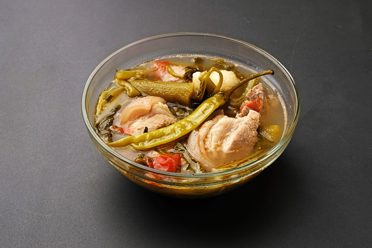 A clear soup with pork pieces and various vegetables in a glass bowl.