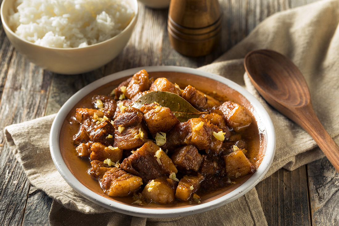 A plate with big meat chunks in a brown liquid, with a bowl of rice on the side.