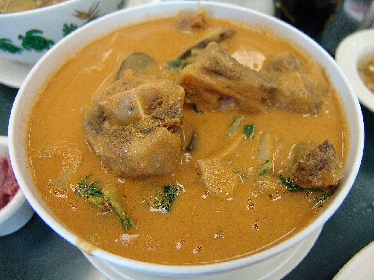 A bowl of orange-coloured soup with meat and vegetables.