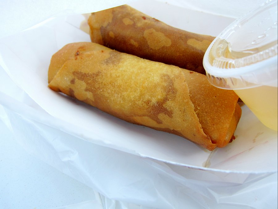 Two fried rolls with a plastic sauce container.