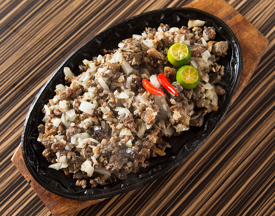 A black plate on a wooden table filled with a meat dish.