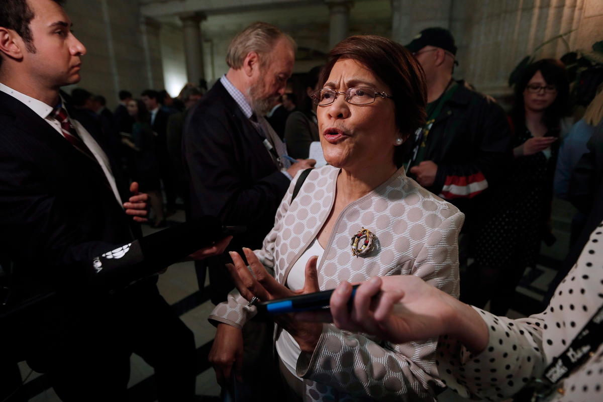 A woman with glasses speaking in a crowd.