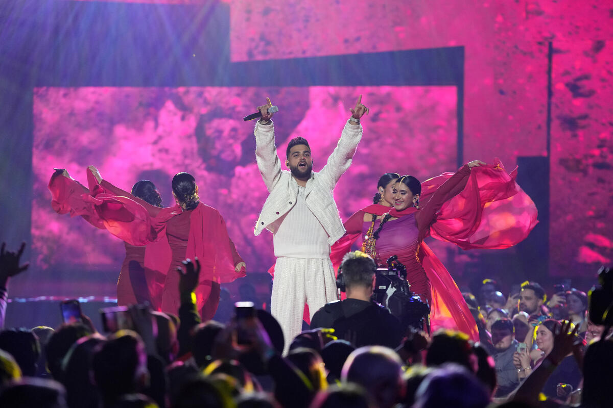 A man dressed in white with dancers in red performing on stage in front of a crowd.