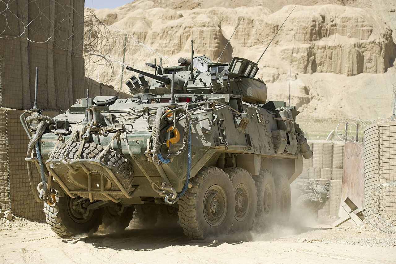 New Zealand LAV A green armoured vehicle leaving a fortified area in an arid environment.