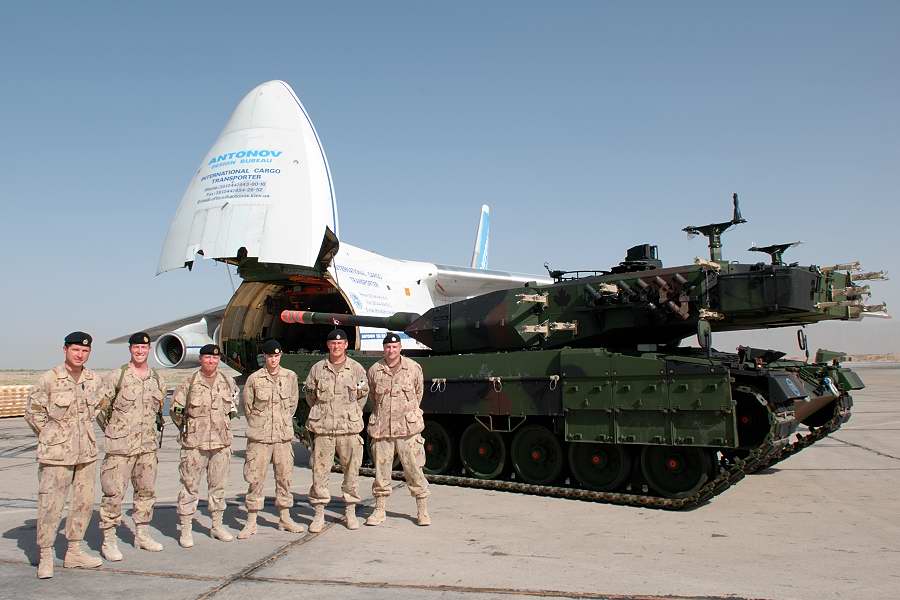 Six soldats à côté d'un Leopard 2 vert avec un avion à l'arrière.