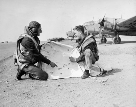 Compter les coups [matériel graphique]: deux équipiers non identifiés examinant un parachute cible à l'École d'artillerie et de bombardement No. 10, RCAF. Canada.