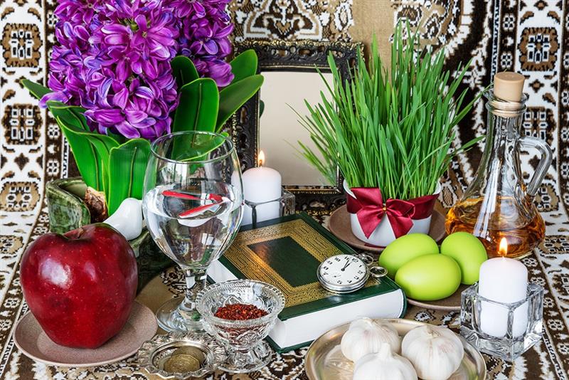 Table de Haft Sîn Plusieurs objets placés côte à côte, notamment un livre, des œufs peints, une pomme, de l'ail, des fleurs et deux bougies.