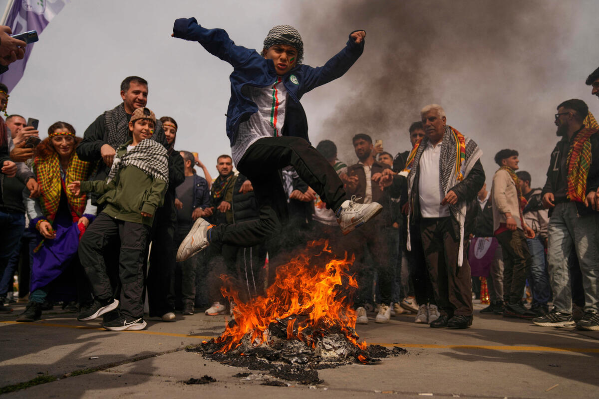 Des Kurdes célèbrent le Norouz Un garçon saute par-dessus d'un feu. Il est entouré d'une foule.