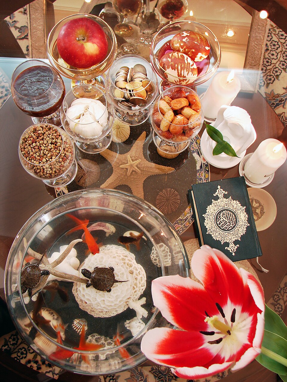 Table de Haft Sîn Plusieurs objets posés sur une table de couleur marron, notamment un livre, de la nourriture, une fleur rouge et blanc et de petites tortues.