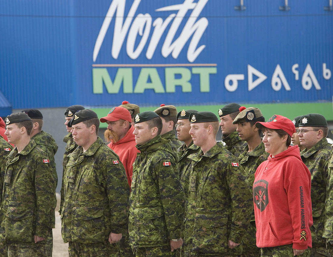 Members of the Canadian Military and Canadian Rangers stand at attention in front of a building in Iqaluit, Nunavut