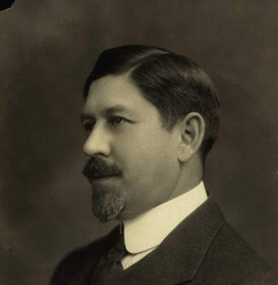 A monochromatic picture of a man in a suit with short hair, a beard, and a mustache.