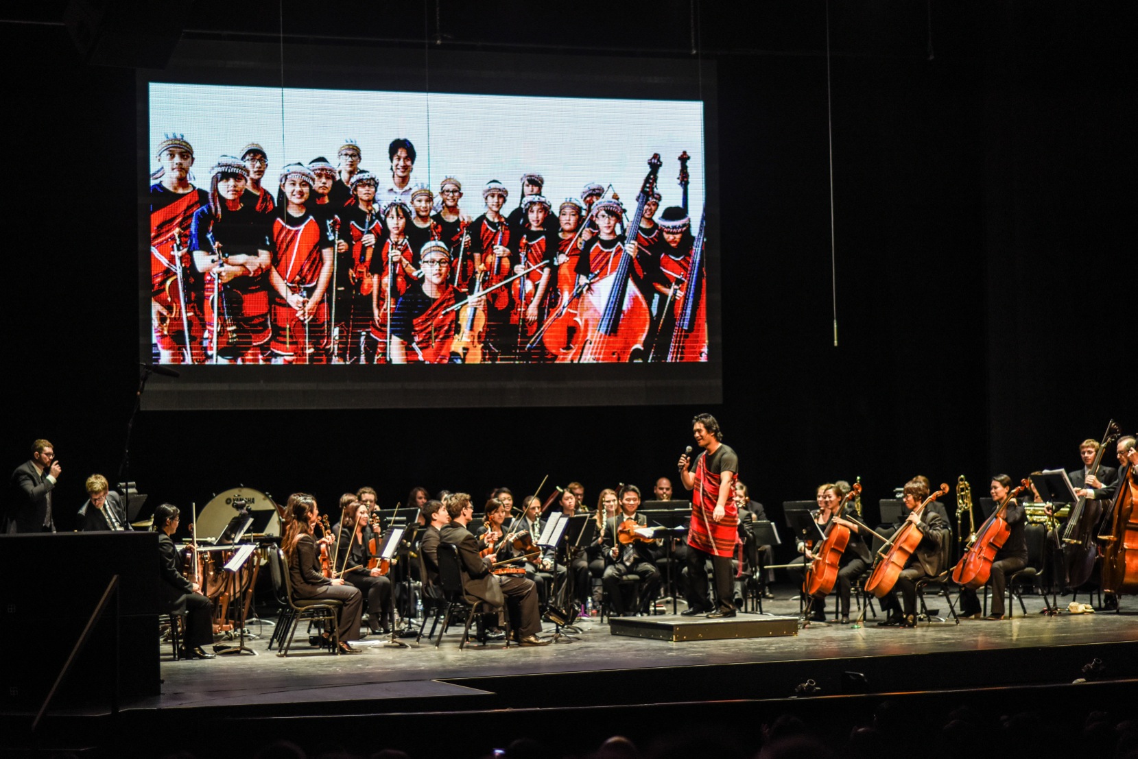 An orchestra on stage with a screen in the background