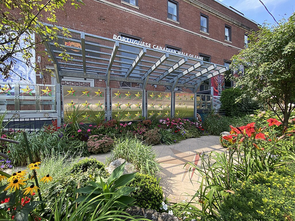 A metal structure with golden stars alongside a garden and a red brick building. 