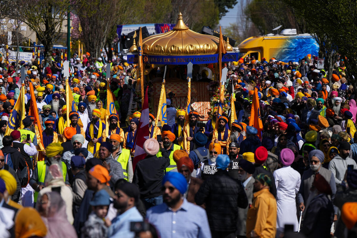 A crowd of people marching alongside a float. Some are carryings yellow and orange flags.