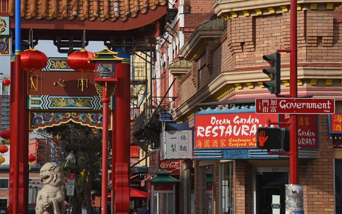 A number of business signs alongside a big Chinatown gate and a stone lion.