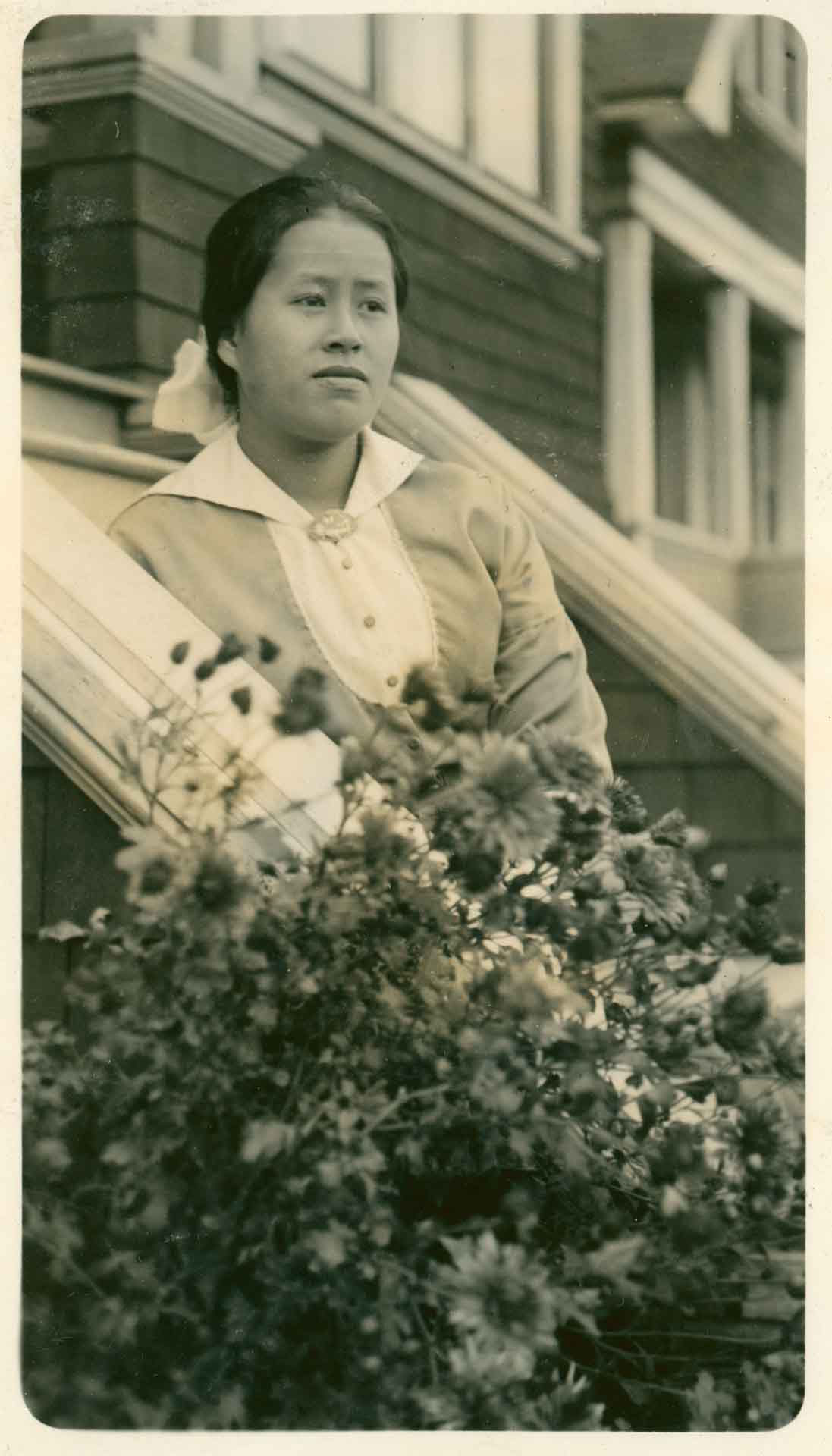 Victoria Chung (1917) A Chinese woman by some flowers and on some steps in front of a building.