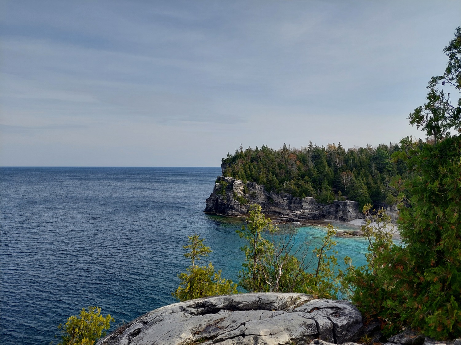 Niagara Escarpment in Bruce Peninsula Rocky cliff by bright blue water.