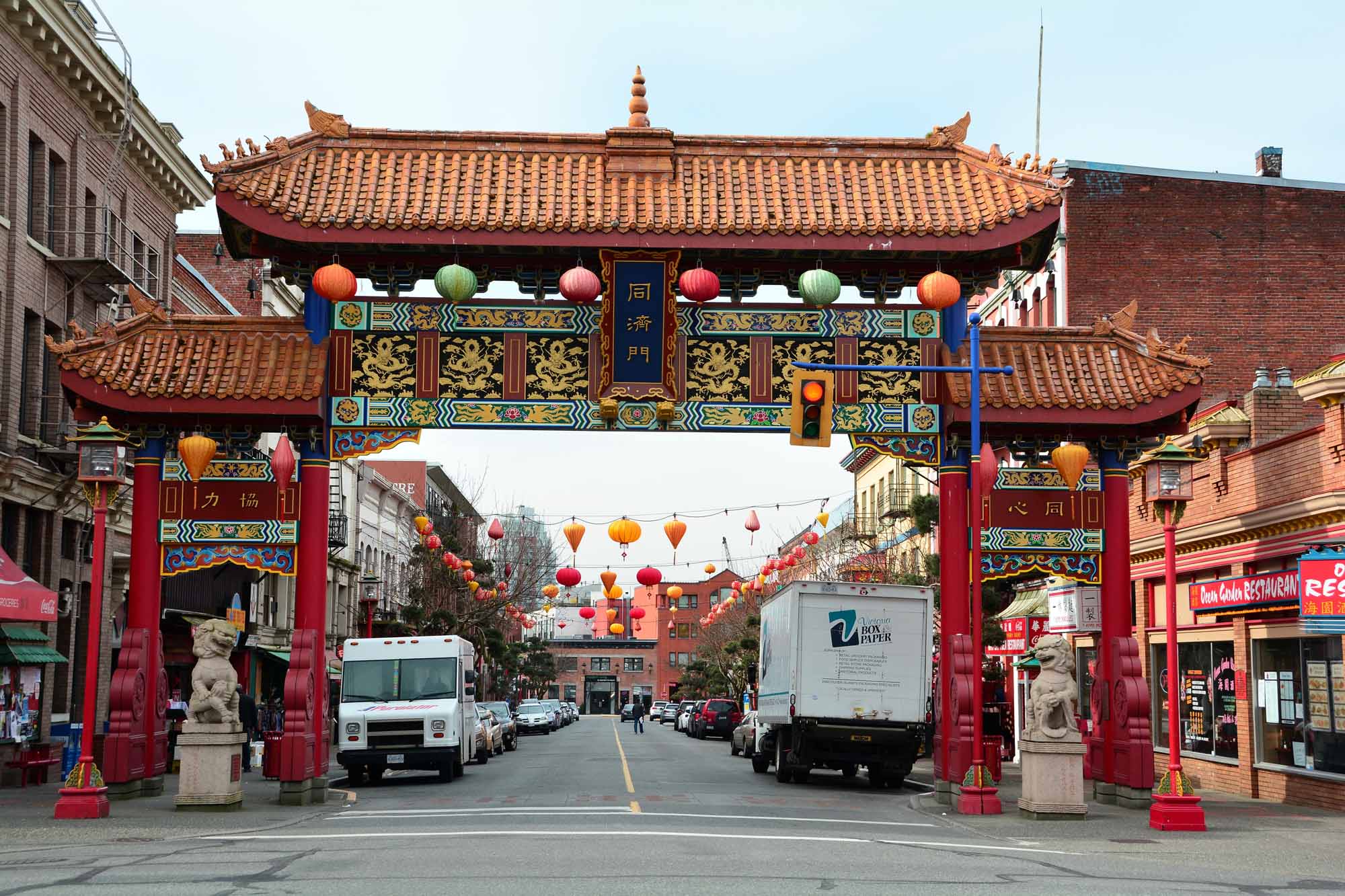 A Chinatown gate with a stone lion on each side. Behind it, there is a street with parked cars and trucks.