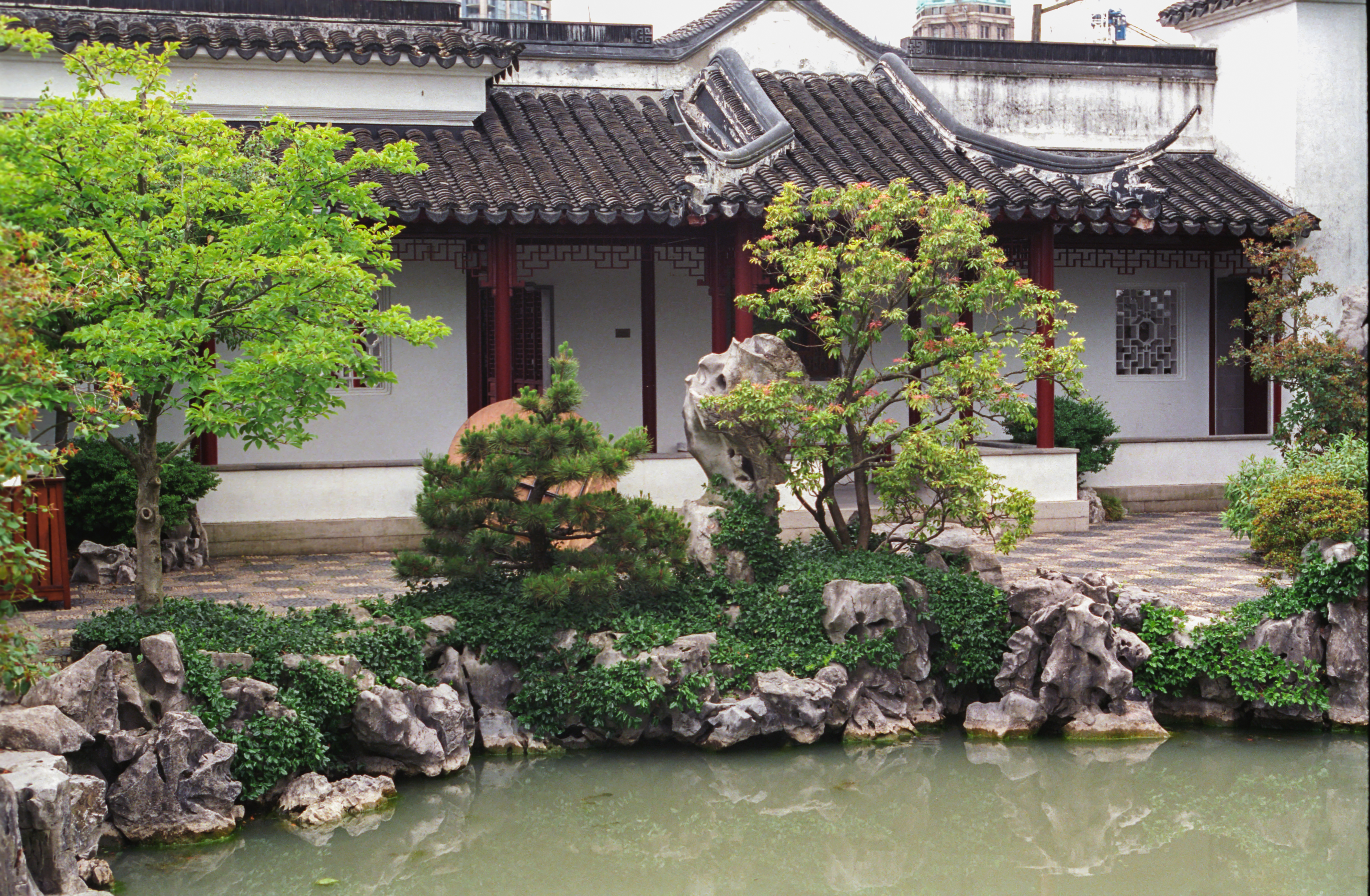 Un bâtiment de style architectural chinois traditionnel derrière des arbres, des rochers et un étang.