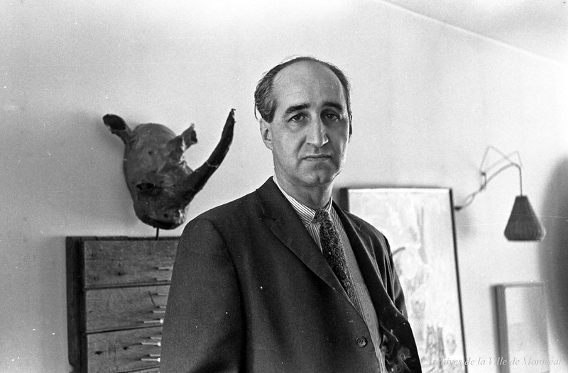 Jacques Ferron Photo en noir et blanc d'un homme en costume et cravate dans une salle.