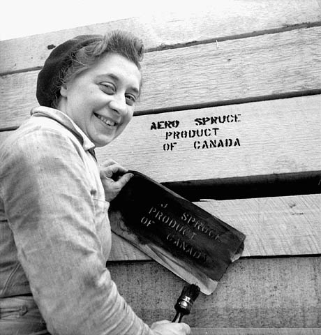 Une bûcheronne non identifiée peint « Aero Spruce Product of Canada » sur une pile de billes au moyen d'un pochoir, avril 1943.