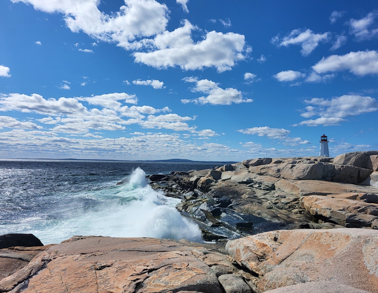 Granite along a shoreline with a lighthouse in the distance.
